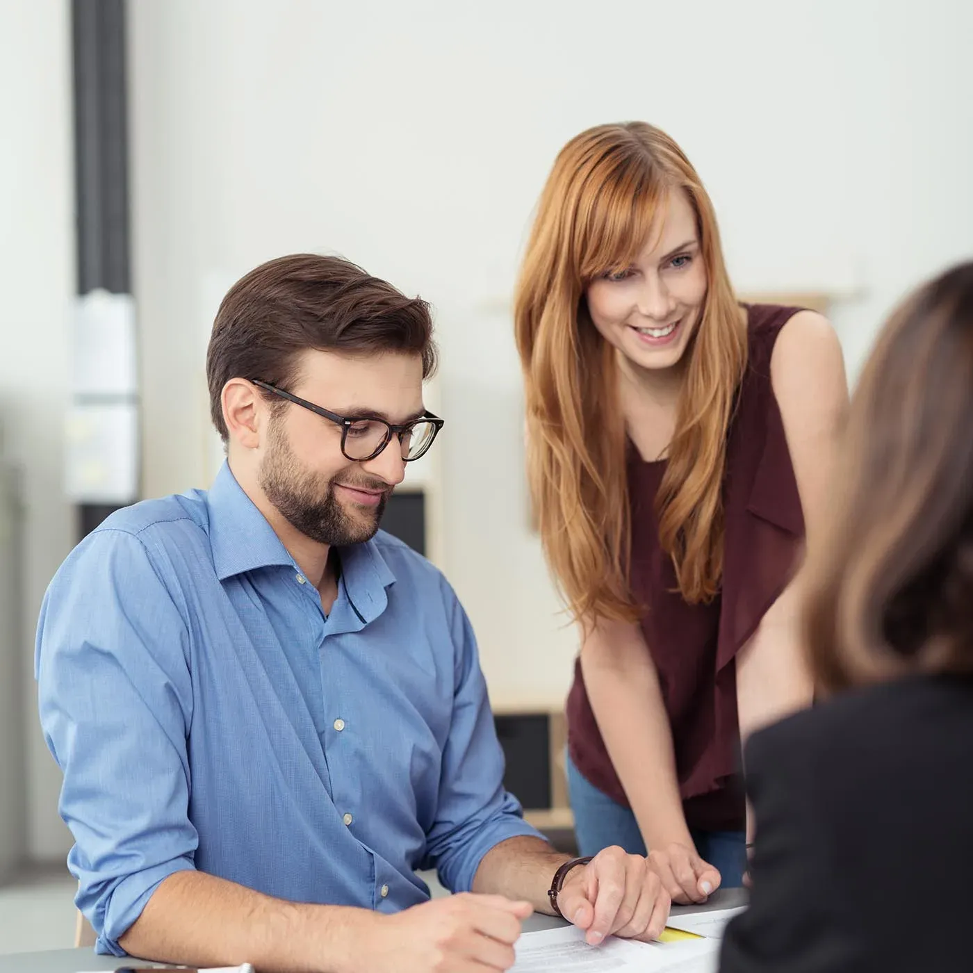 Drei Mitarbeitende am Besprechungstisch sehen gemeinsam auf ihre Unterlagen