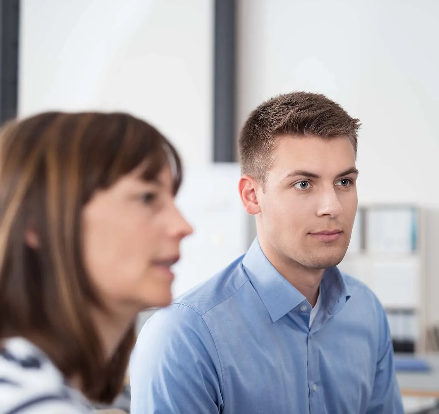 Zwei Mitarbeitende in einem Büro, vorn eine Frau im Gespräch, dahinter ein Mann am Schreibtisch